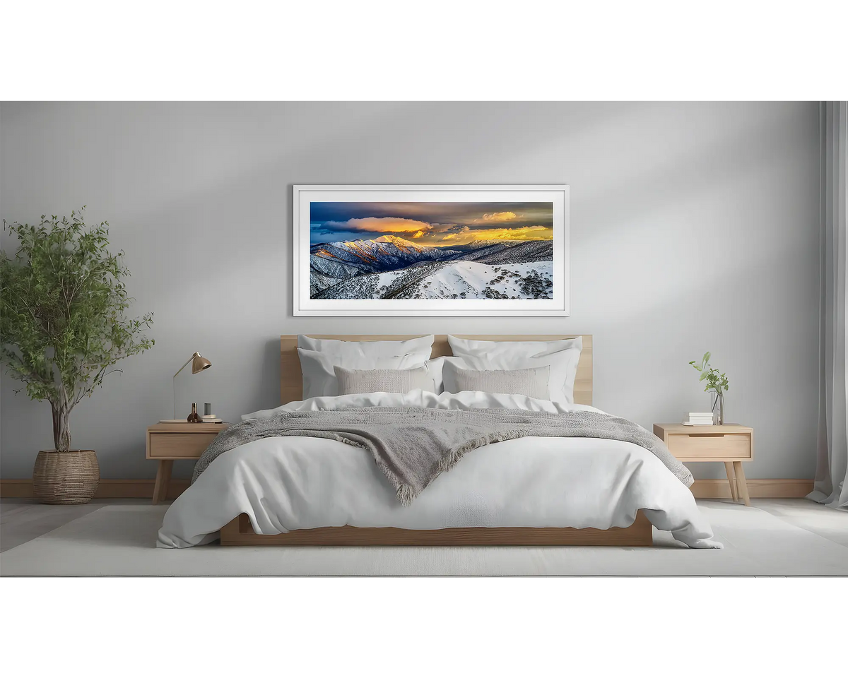 Alpine Magic. Winter snow sunrise wall art, in a white frame, above a bed.