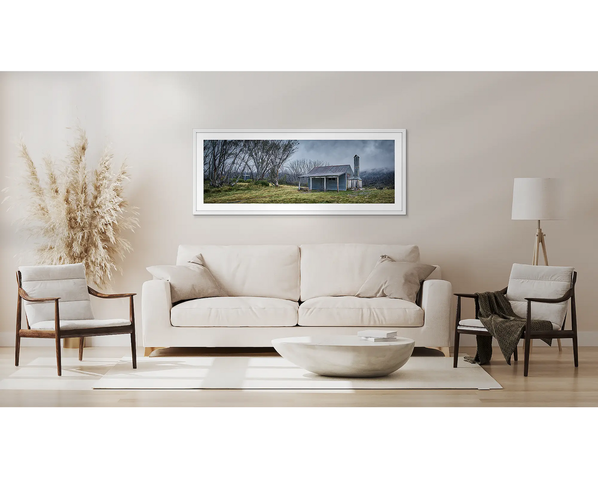 Alpine Retreat. High country hut artwork, in a white frame, above a couch. 