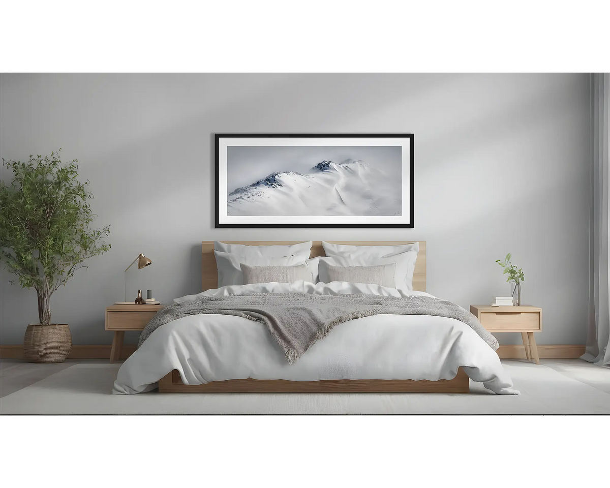 Ascent. Winter snow artwork in a black frame, above a bed. 