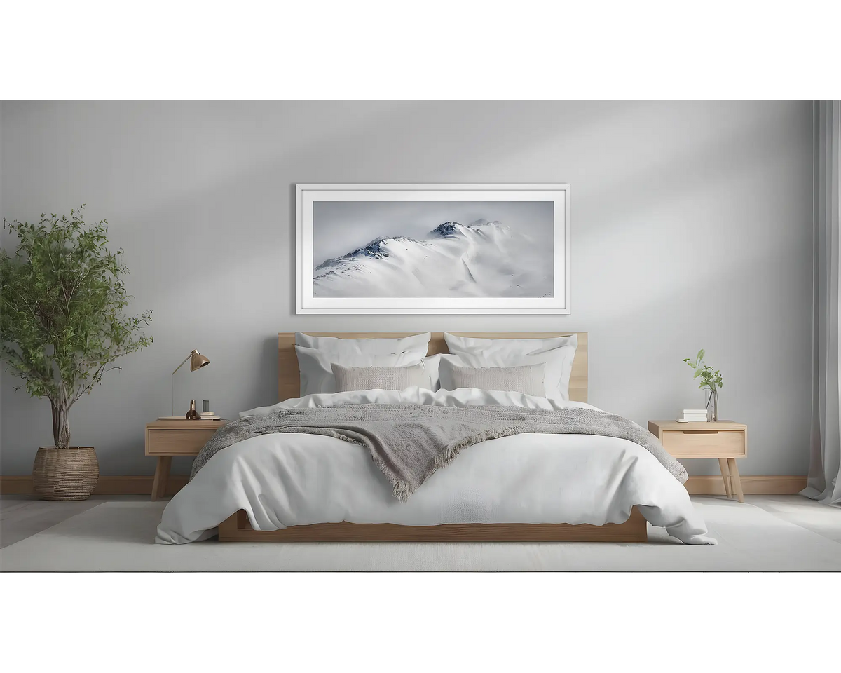 Ascent. Winter snow artwork in a white frame, above a bed. 