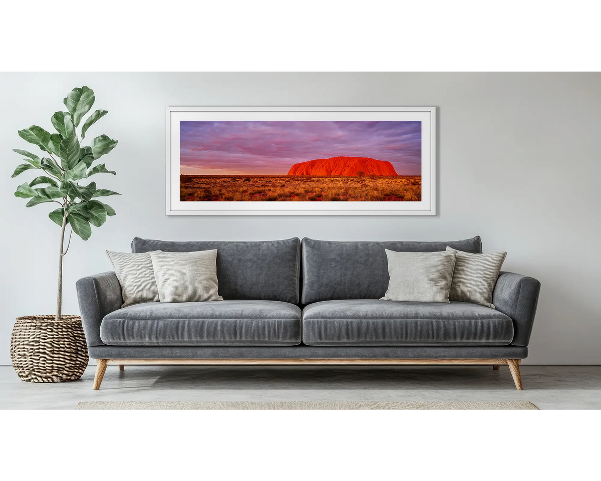 Australian Icon. Uluru wall art, in a white frame, above a grey couch. 