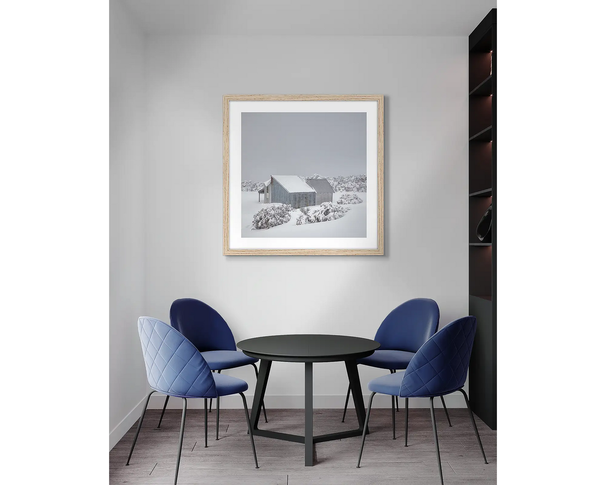 Blowhard. Framed, Alpine hut in snow, artwork with a timber frame, hung above a meeting room table.