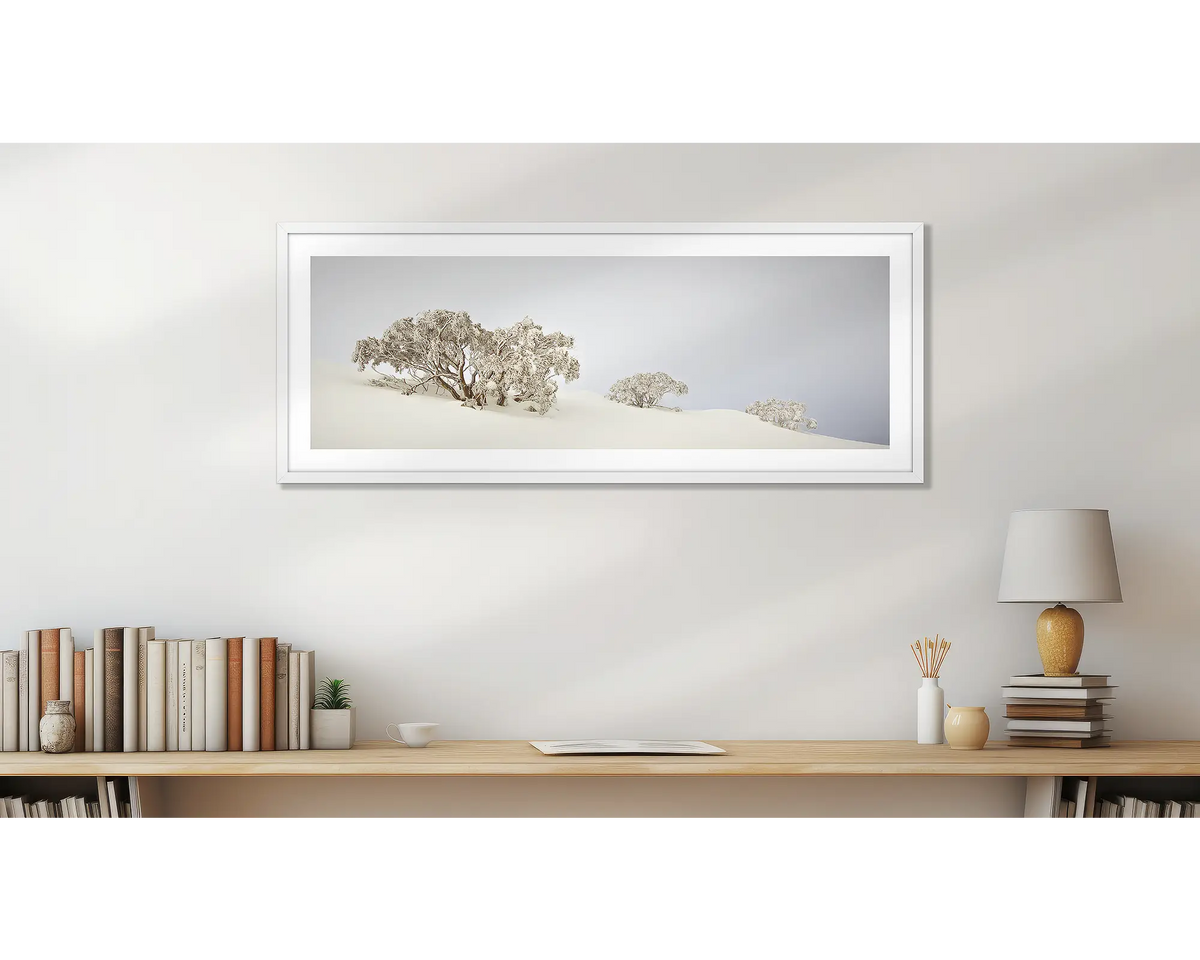 Braving The Elements Winter. Winter snow gums, wall art print, with a white frame, above a desk. 