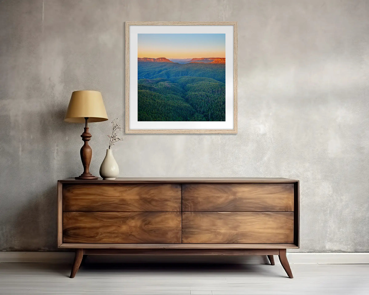 Breaking Dawn. Square, Blue Mountains wall art print, with a Tassie oak frame, above a side table. 