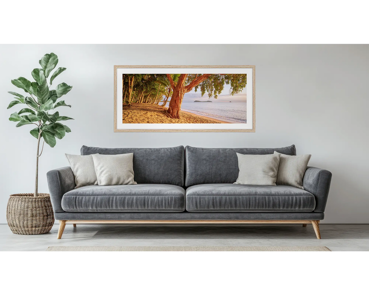 Cairns Escape. Framed wall art print of a sunrise on a tropical beach, with a timber frame, hung above a couch.