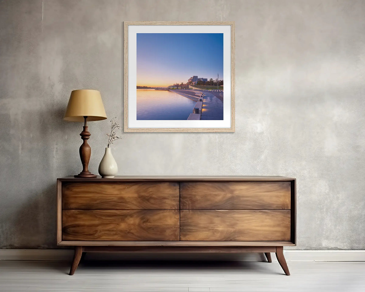 Canberra Awakes. Square, Canberra wall art print, with a timber frame, above a side table.