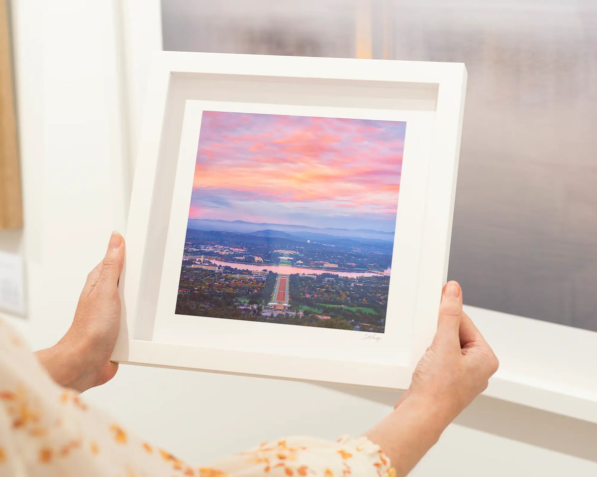 Colours of Canberra. Anzac Parade at sunrise, small framed print with white frame being held.