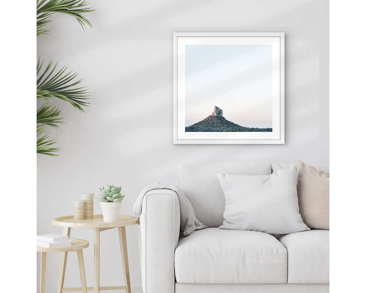 Crookneck. Framed Glasshouse Mountains wall art print, with a white frame, hung above a couch.