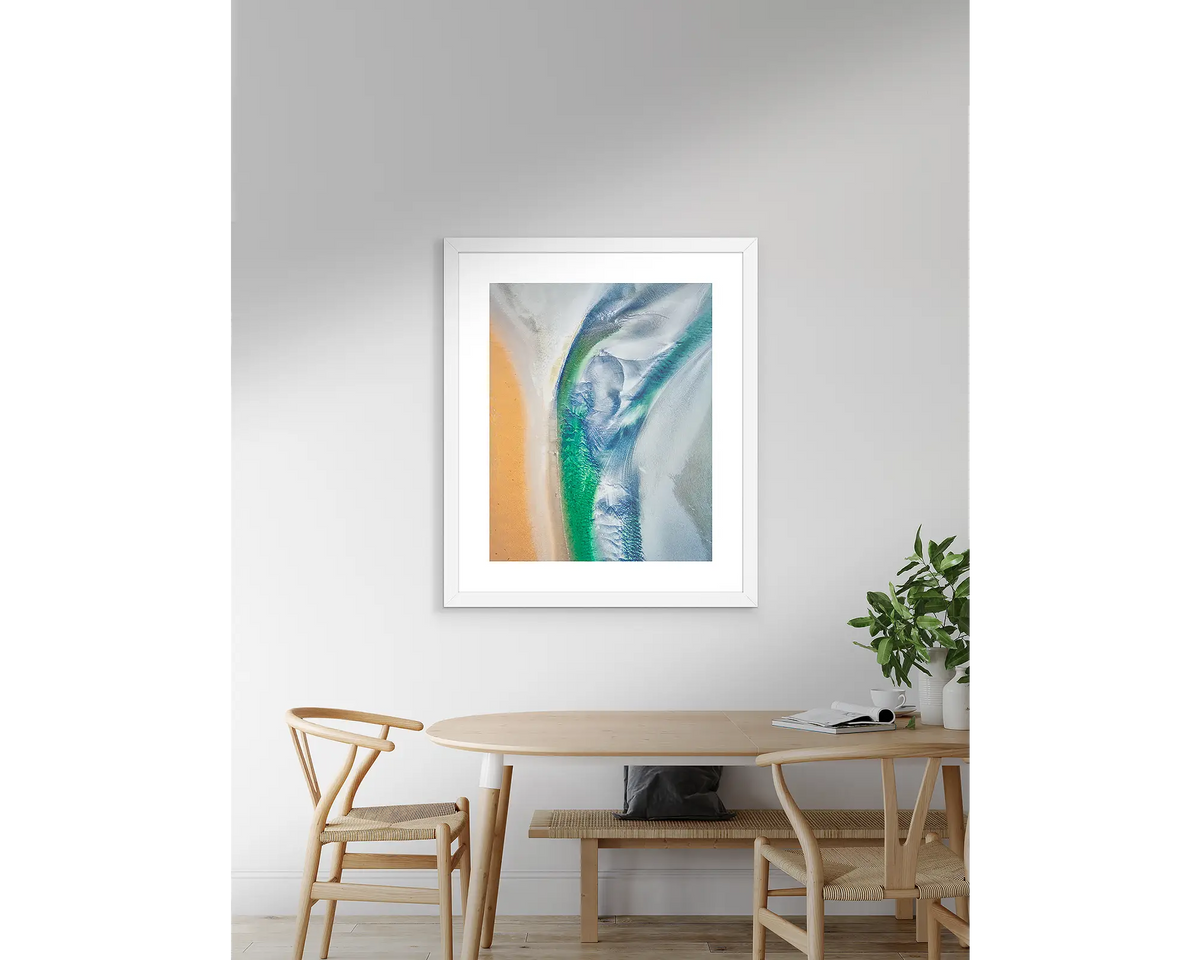 Displacement aerial abstract wall art print with white frame, hanging on wall above table.
