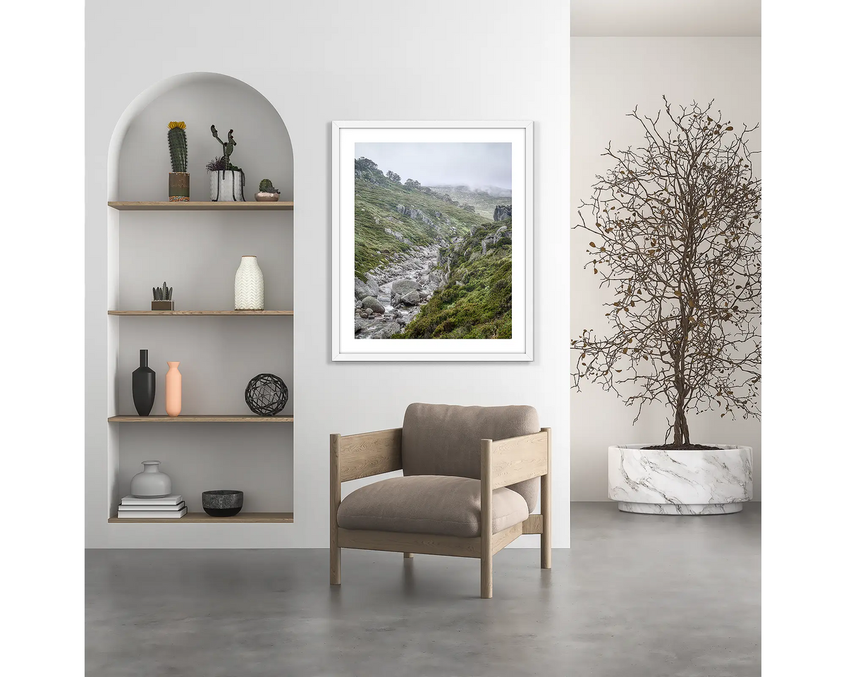 Downstream. Snowy River wall art print, with a white frame, hung above a chair.