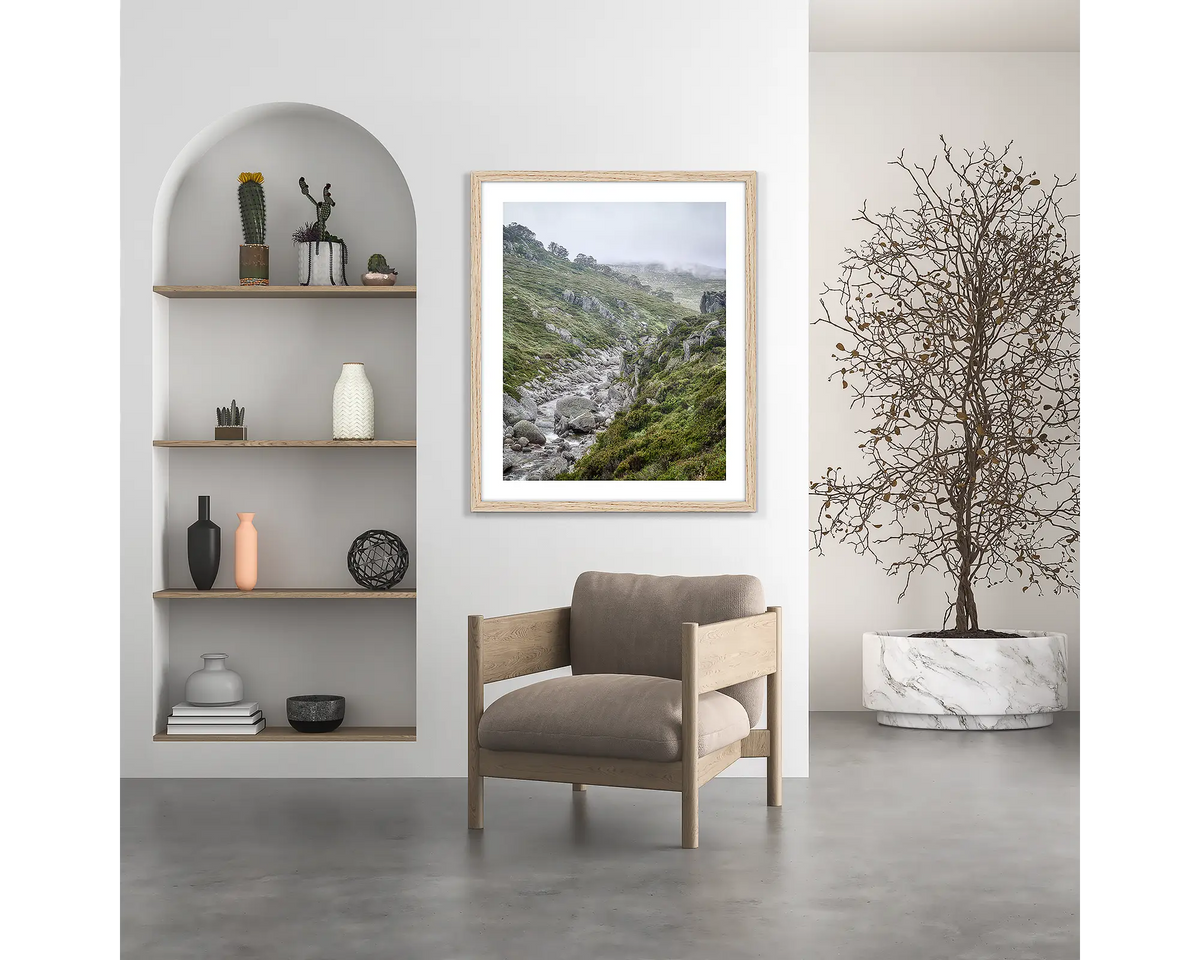 Downstream. Snowy River wall art print, with a wood frame, hung above a chair.