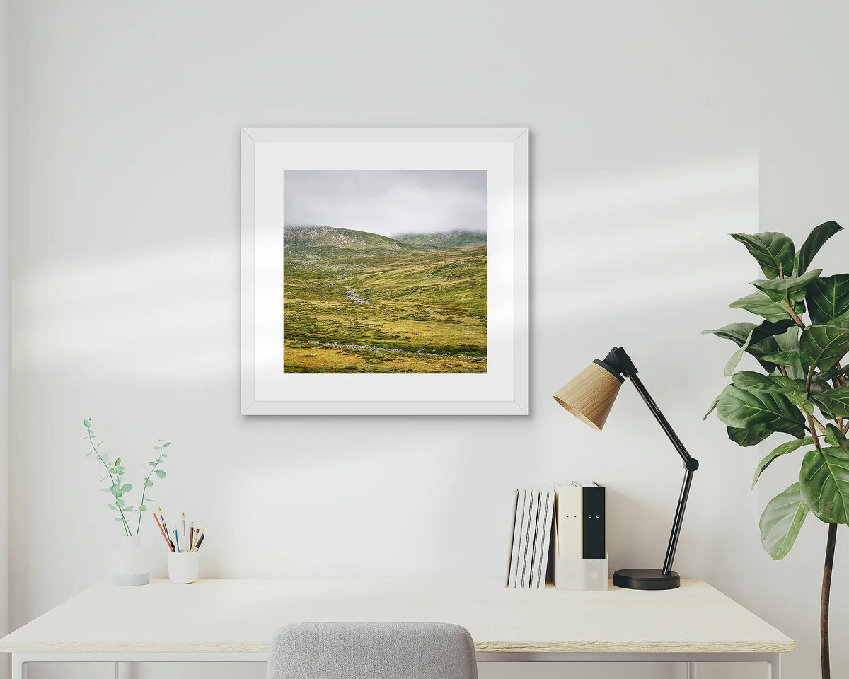 Drizzle. Snowy Mountains framed artwork, with a white frame, on a study wall. 