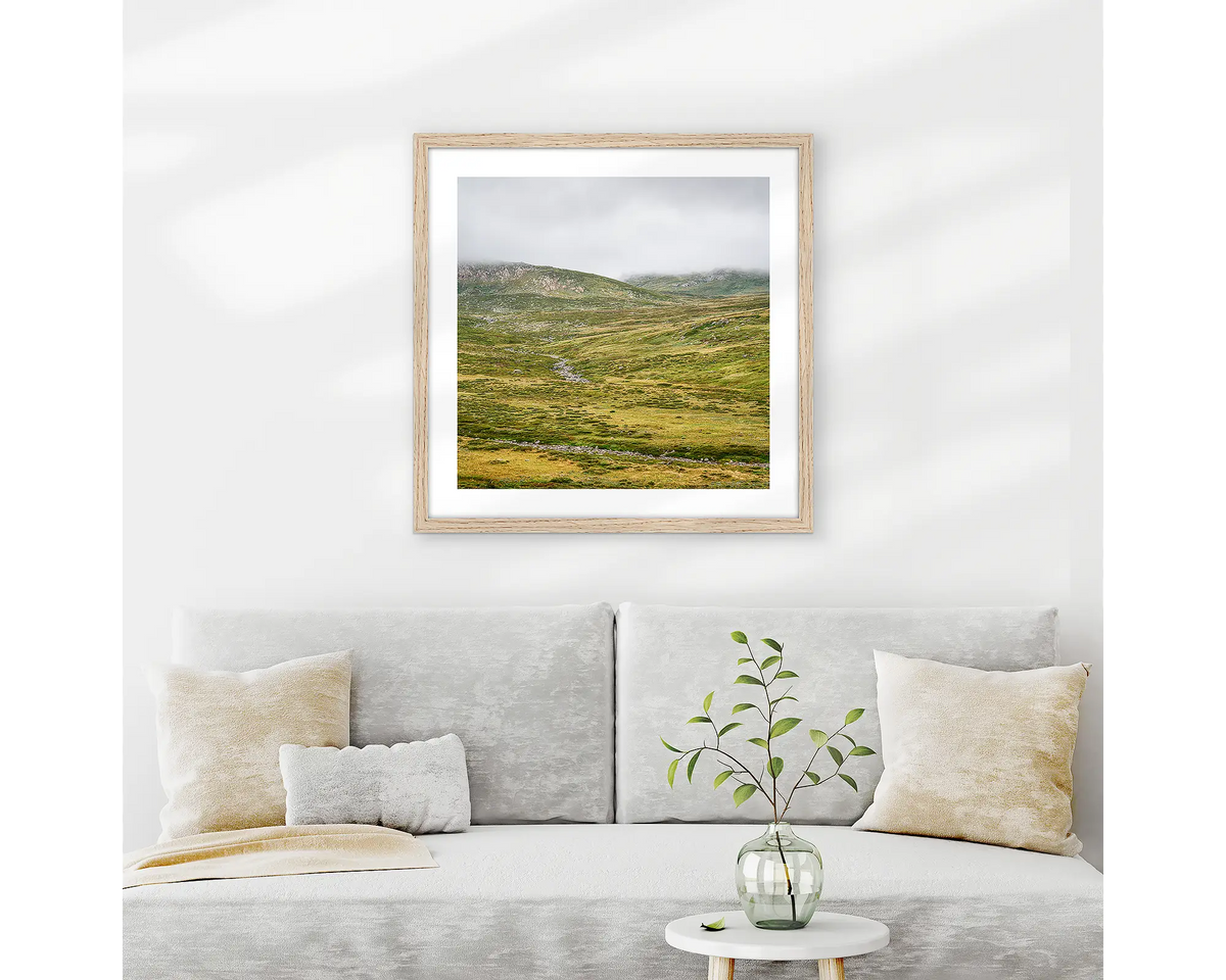 Drizzle. Snowy Mountains wall art print with wood frame hung above couch.