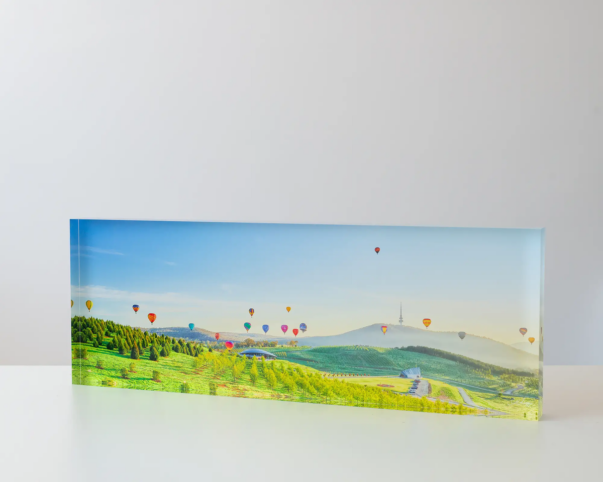 Enlighten. Acrylic block of hot air balloons at sunrise over the National Arboretum. Canberra artwork on table.