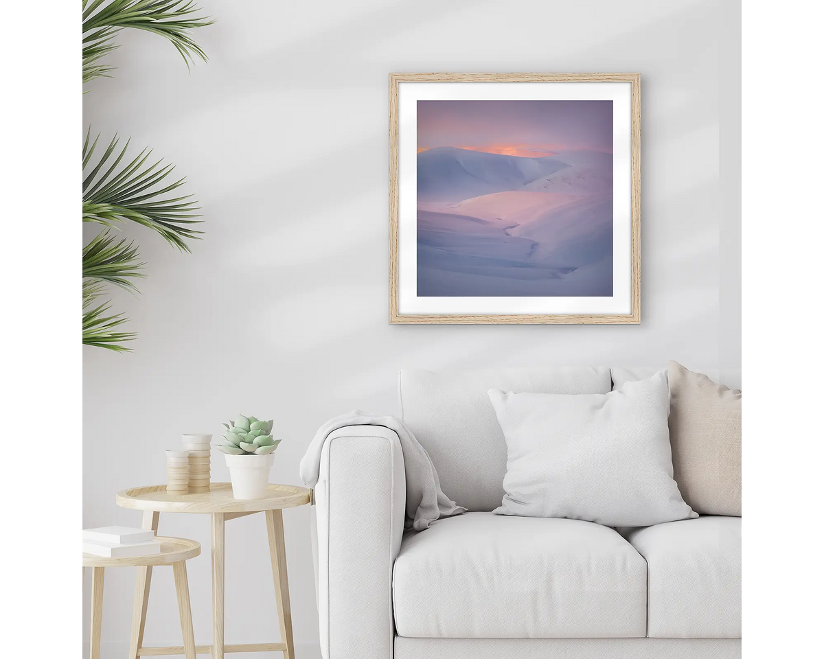 Essence of the Snowy. Framed Snowy Mountains wall art print, with a timber frame, hung above a couch.