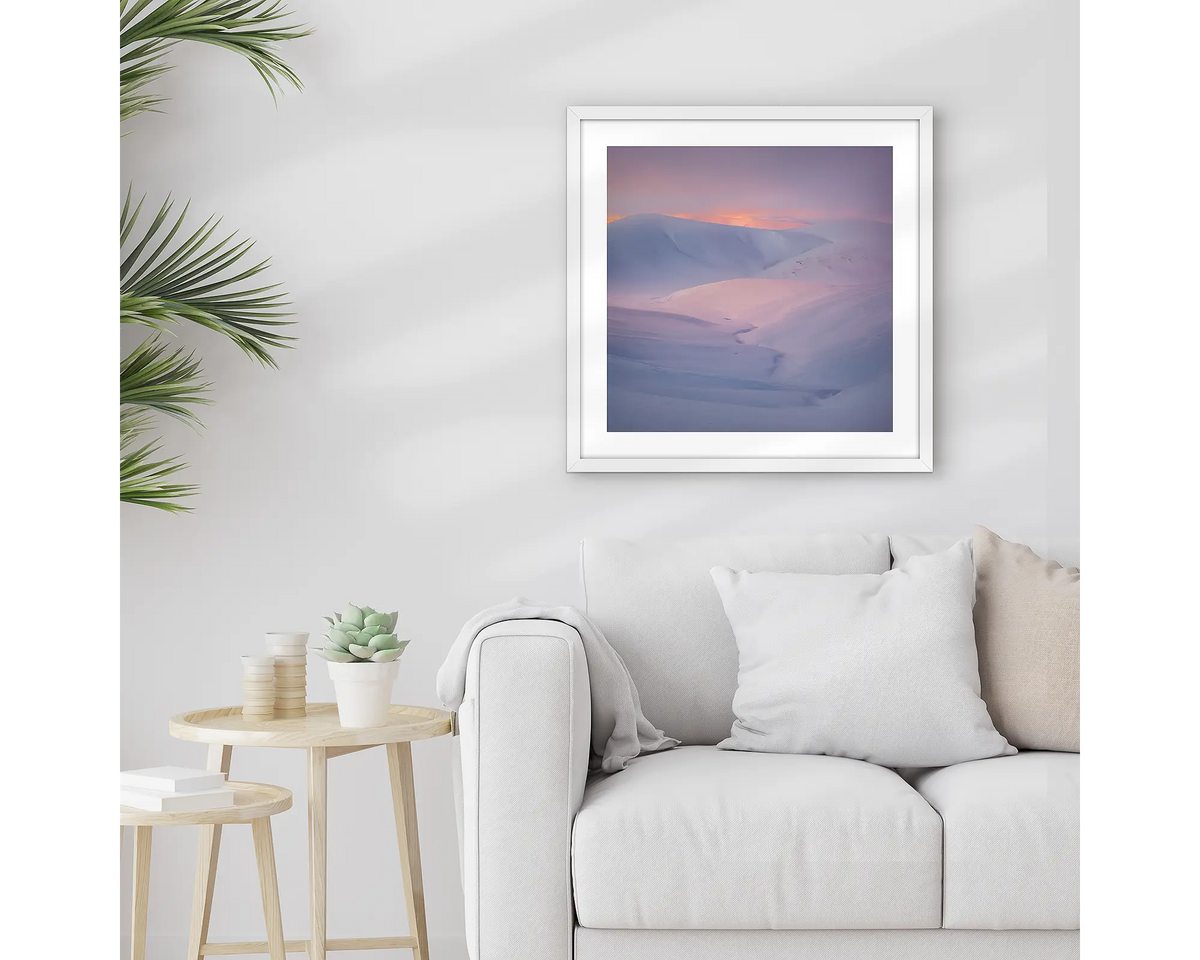 Essence of the Snowy. Framed Snowy Mountains wall art print, with a white frame, hung above a couch.