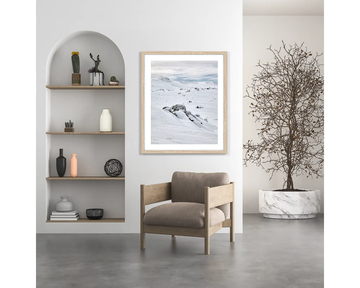 Etheridge Lines. Snowy Mountains wall art print, with a white frame, hung above a chair.