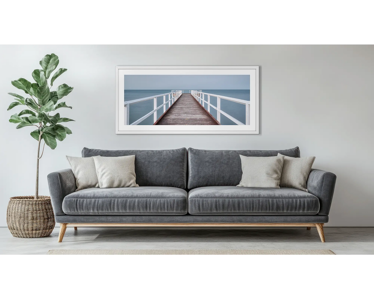 Evening Calm. Framed wall art print of a jetty, with a white frame, hung above a couch.