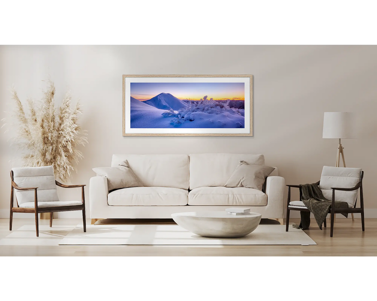 Feathertop Dawn. Alpine snow wall art print, with a Tassie oak frame, above a couch. 