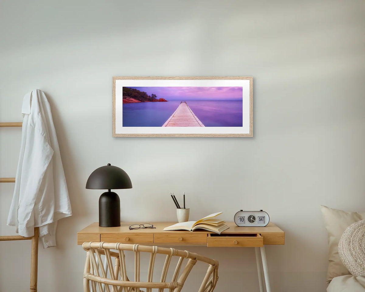 Freycinet Retreat. Jetty at sunrise, Oyster Bay, Tasmania, coastal wall art print with an oak frame, above a bedside table.