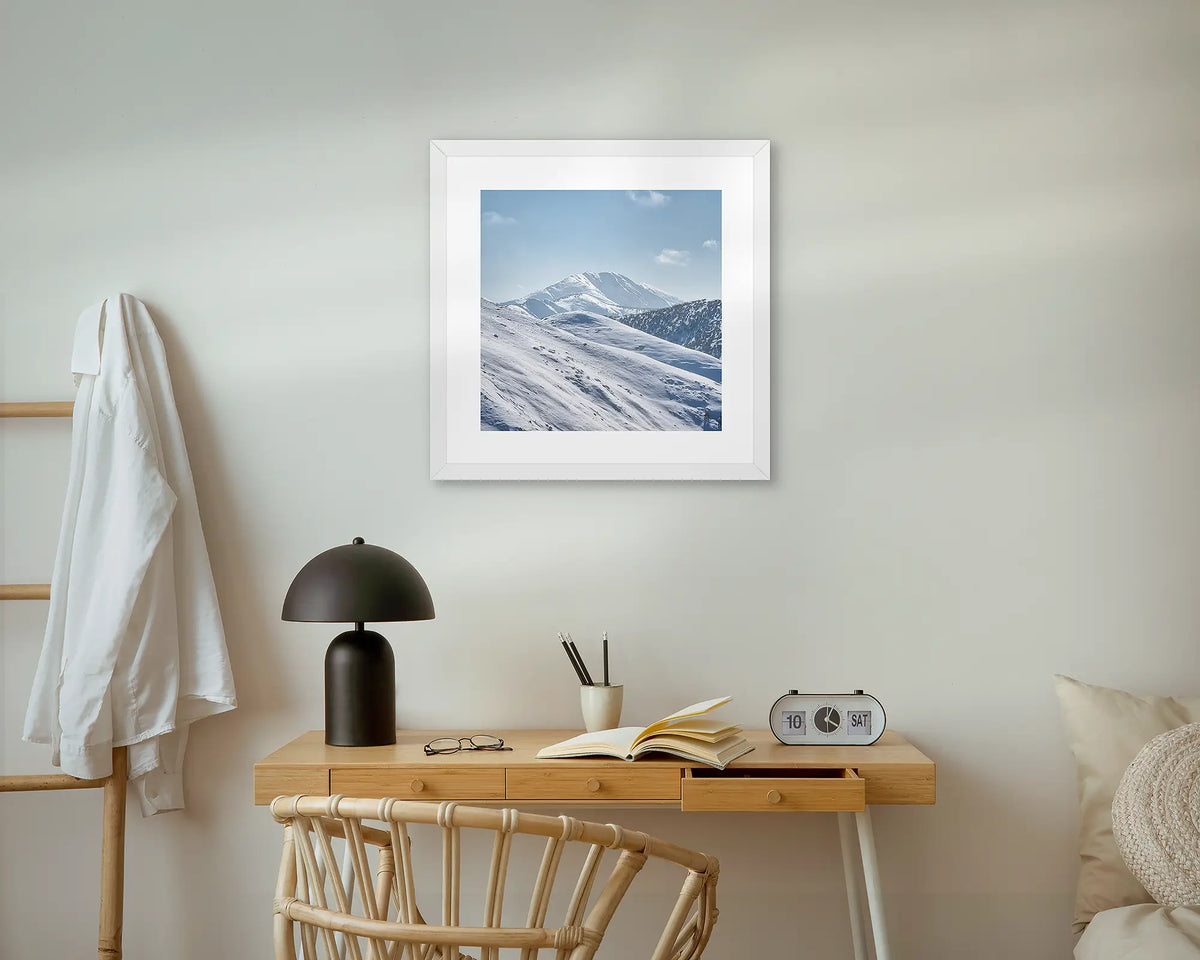 Icon Of The Alps. Mount Feathertop framed wall art print, with a white frame, above a bedside table. 