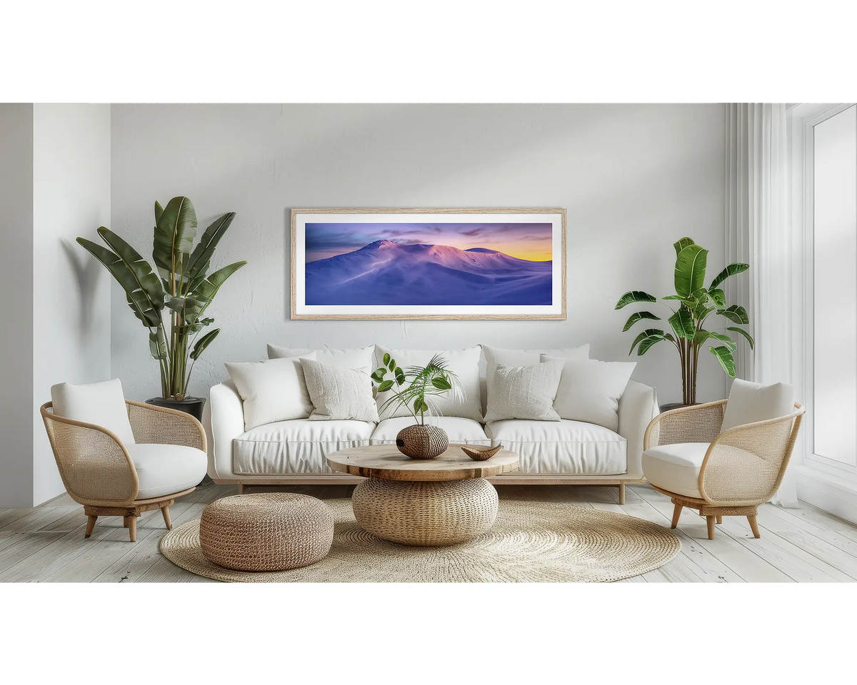 Kosciuszko Dawn. Snowy mountains wall art print, with a Tassie Oak frame, above a couch. 