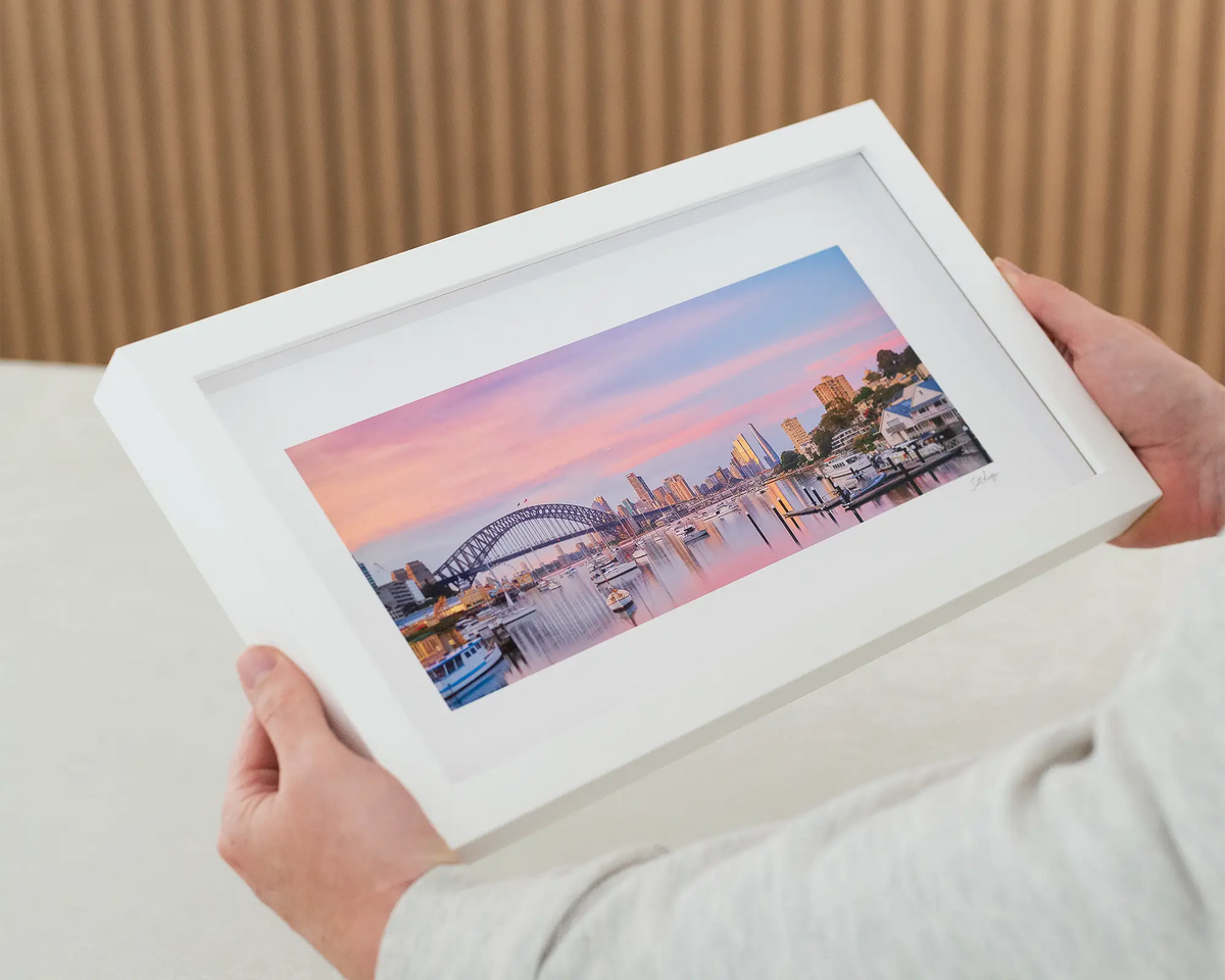 Lavender Sunrise. Pink sunrise over Sydney Harbour Bridge and Lavender Bay, Sydney. Wall art being held. 