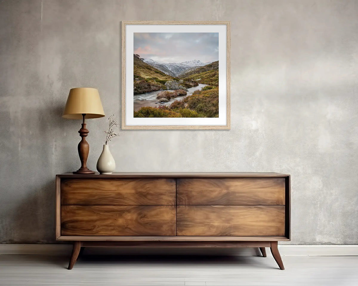 Looking Up. Square, Thredbo river wall art print, with a Tassie oak frame, above a side table.