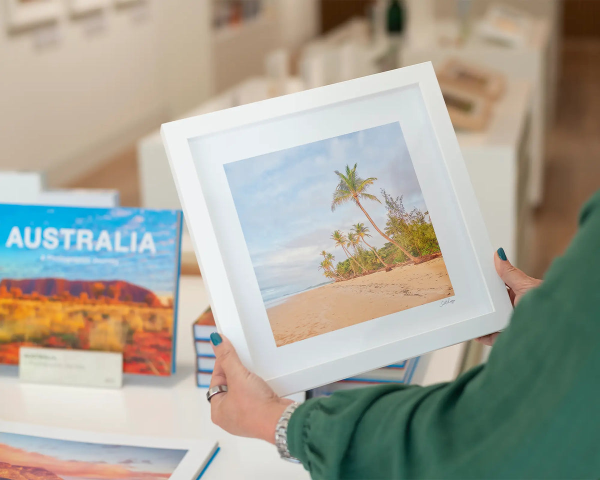 Mission Palms. Picturesque beach, small square framed print with a white frame, and a book.