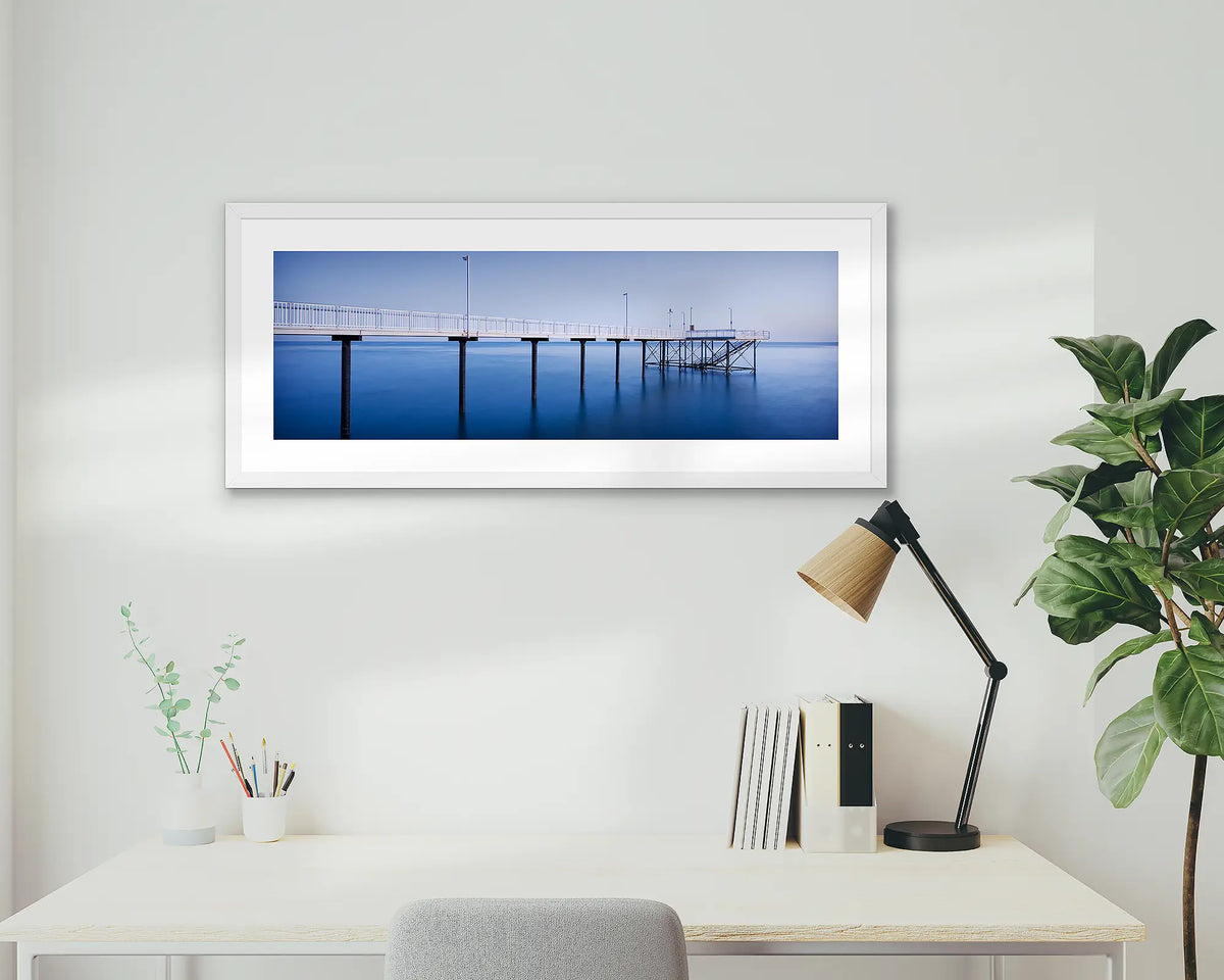 Nightcliff Jetty. Darwin sunrise, framed wall art print, in a white frame, hanging above a desk.