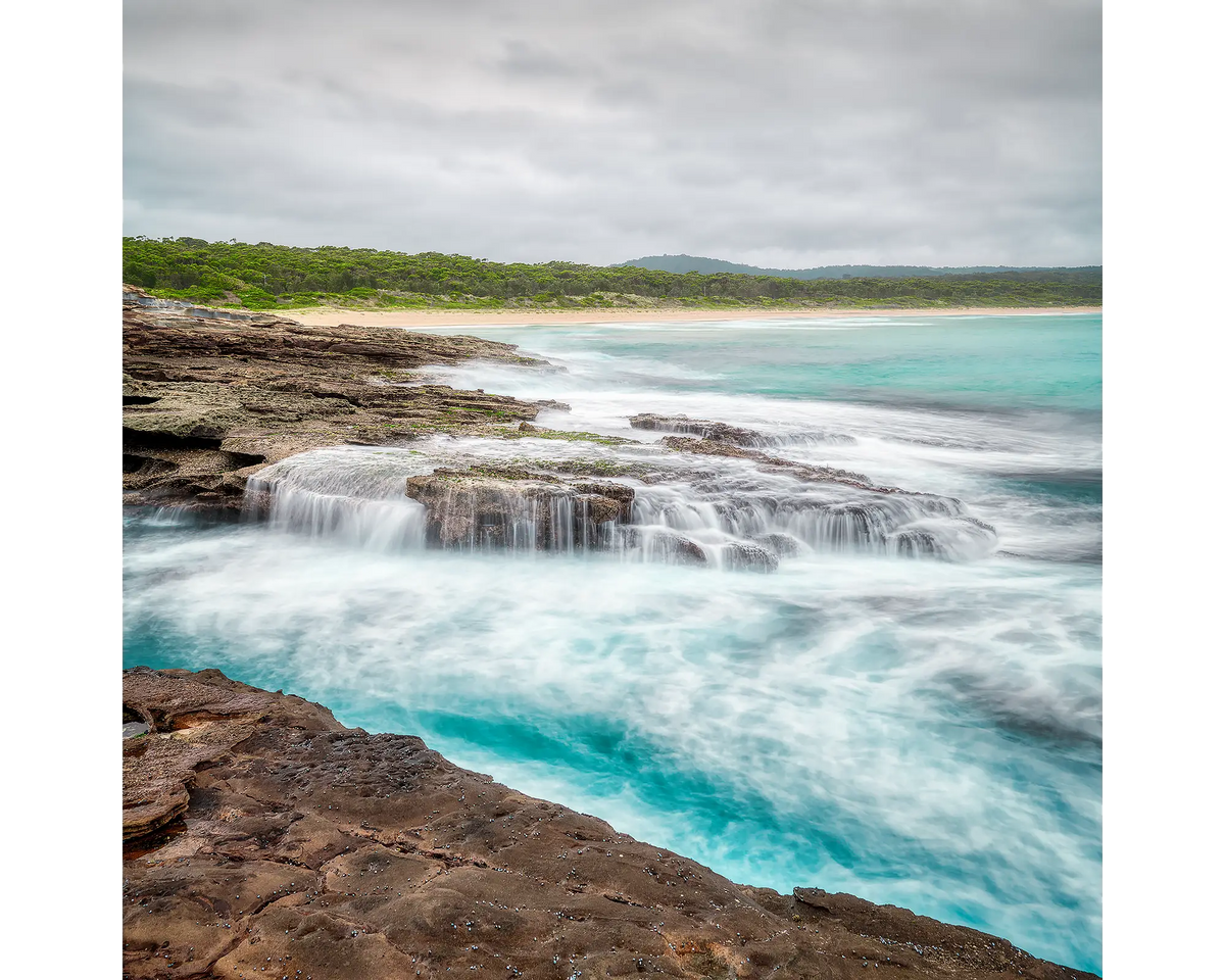 Waves crashing over rocks at South Durras Beach with rain clouds overhead, Eurobodalla, NSW. 