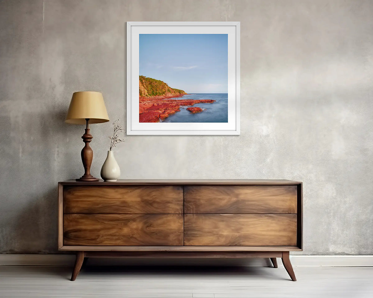 Point. Square, Merimbula wall art print, with a white frame, above a side table. 