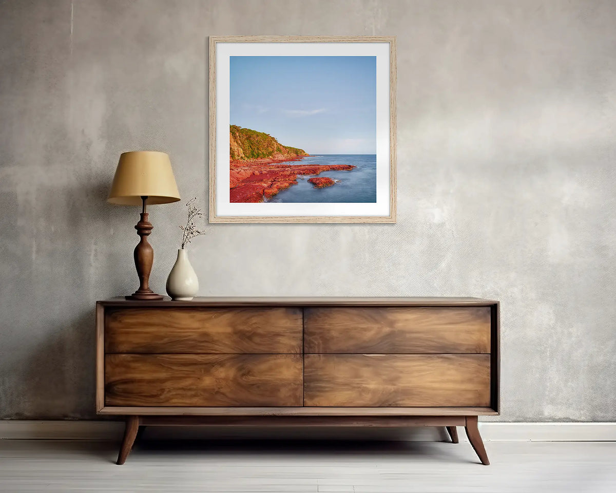 Point. Square, Merimbula wall art print, with a wood frame, above a side table. 