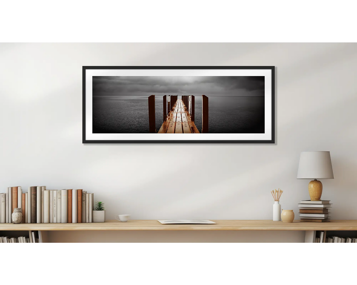 Rain Over Geographe Bay. Wall art print of a jetty, with a black frame, in a home study. 