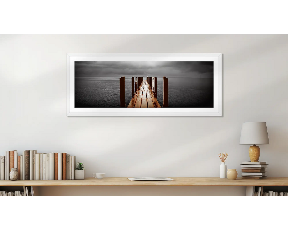 Rain Over Geographe Bay. Wall art print of a jetty, with a white frame, in a home study. 