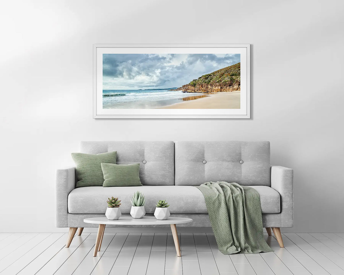 Rolling In. White framed coastal wall art above a couch. 