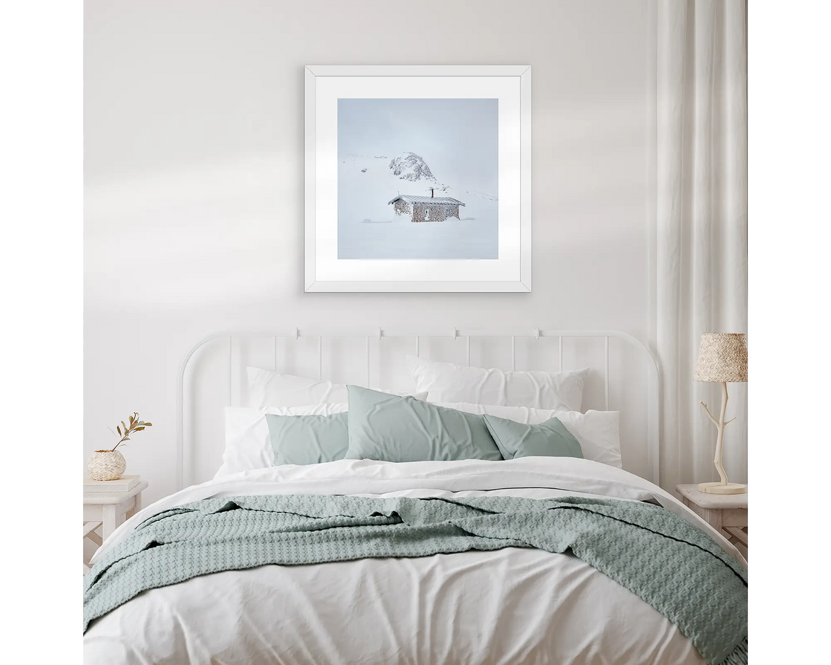 Seamans Hut. Snowy Mountains artwork hanging above a bed, with white linen.