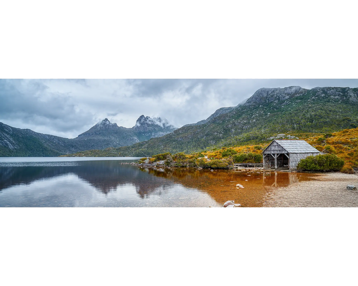 Clouds lingering above an old boat shed on the shore of Dove Lake, with Cradle Mountain in the background. 