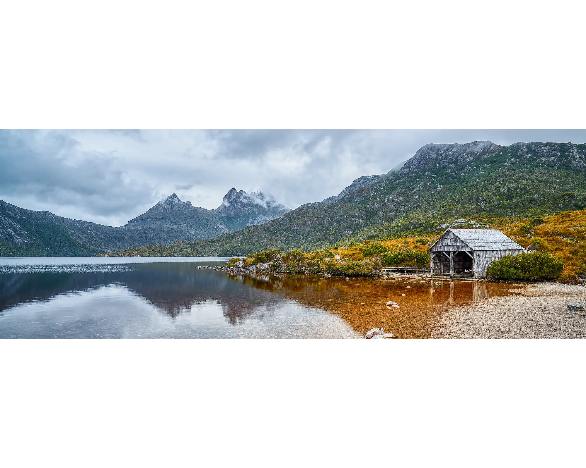 Clouds lingering above an old boat shed on the shore of Dove Lake, with Cradle Mountain in the background. 