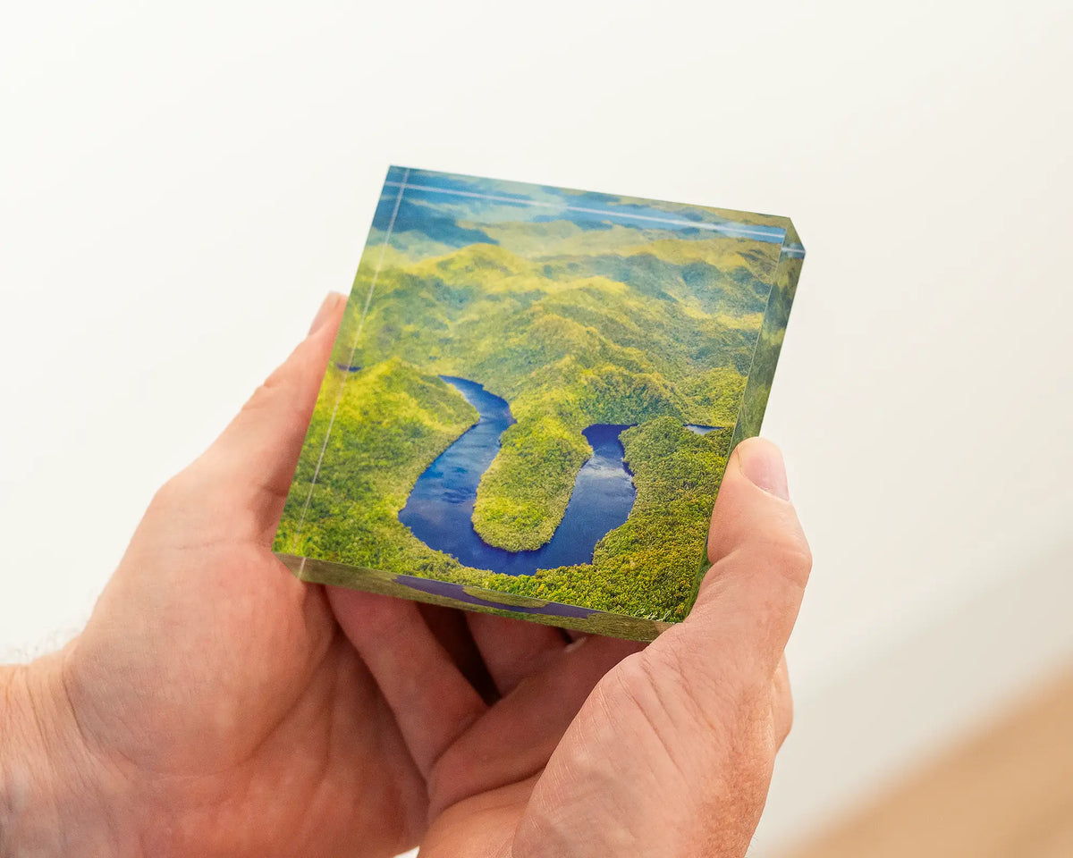 Acrylic block with an image of a river winding through a forest inside of it being held in hands. 