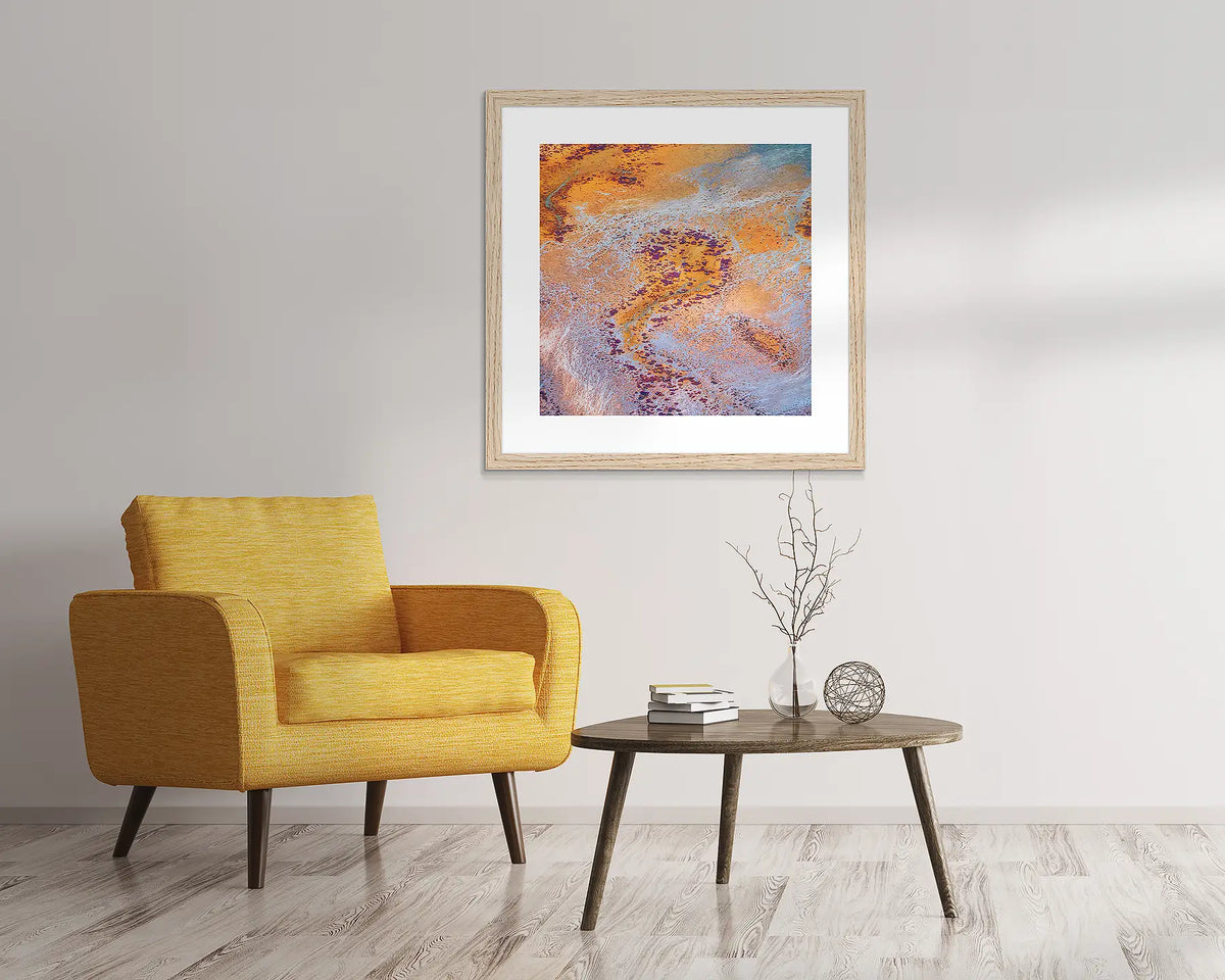 The Chase. Abstract Kimberley wall art in a Tasmanian Oak frame, hanging above a yellow chair.