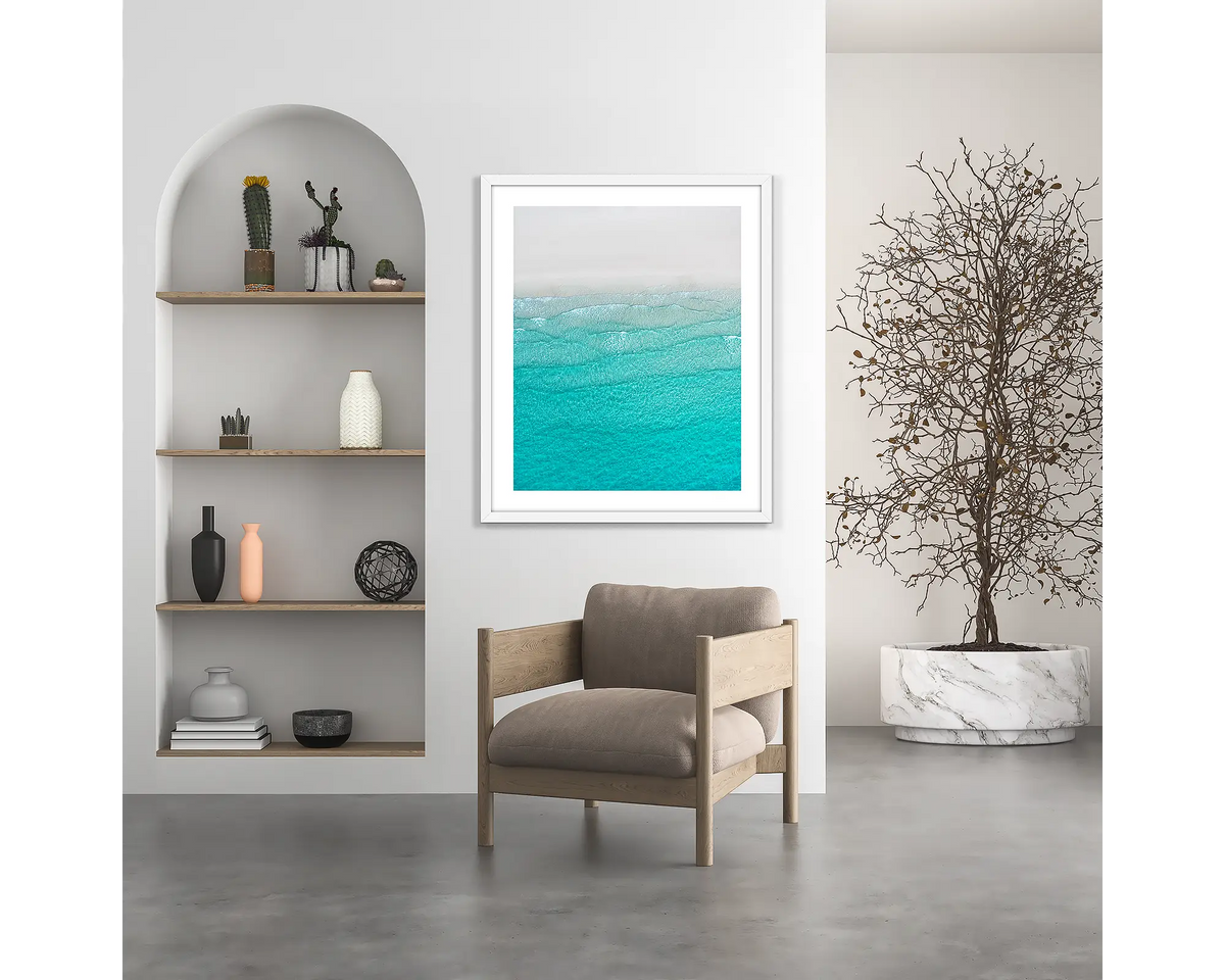 Tranquility. Coastal wall art print, with a white frame, hung above a chair.