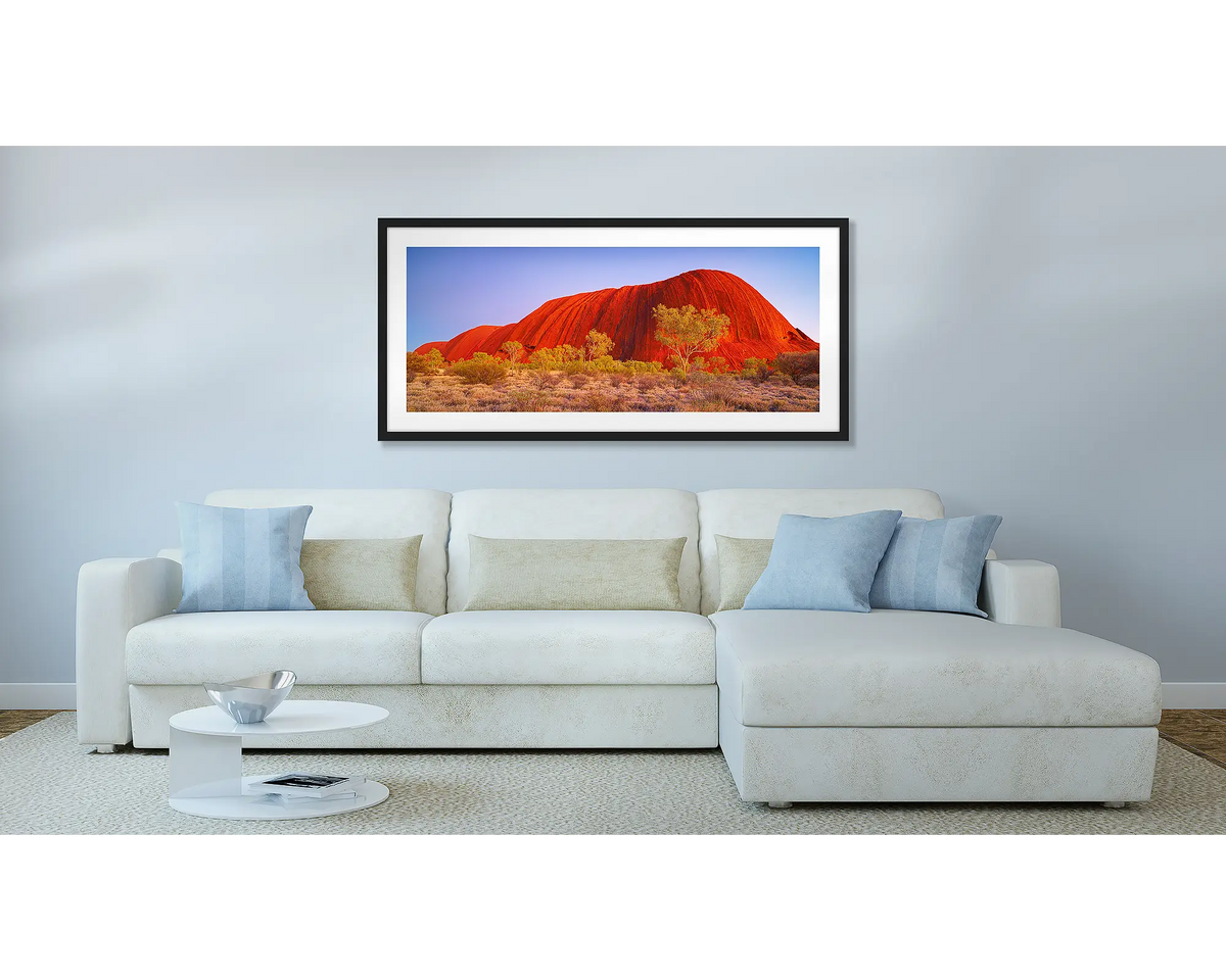 Uluru Awakening. Outback wall art print, with a black frame, hung above a couch.