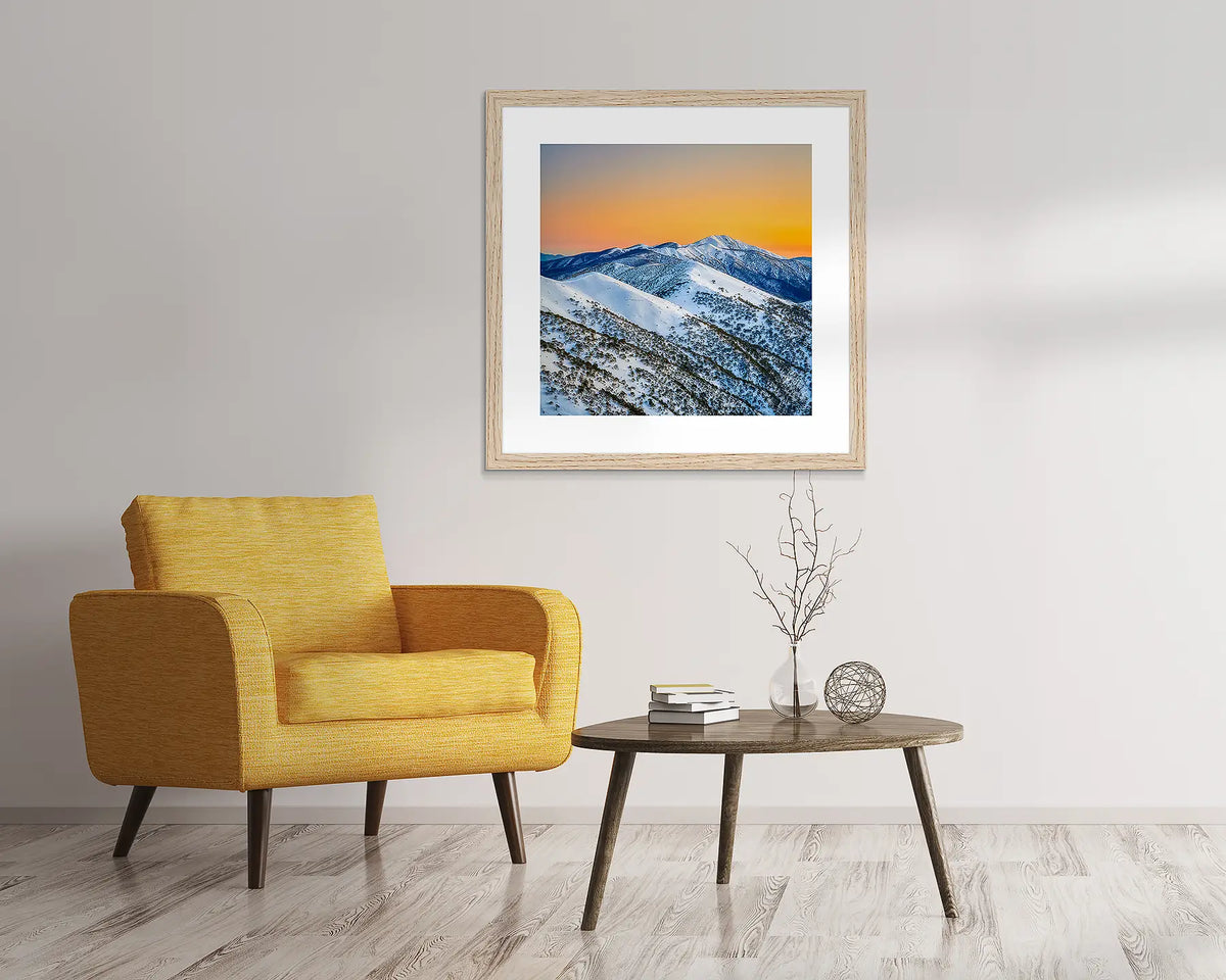 Winter Glow snow wall art in Tasmanian Oak frame, hanging above yellow chair.